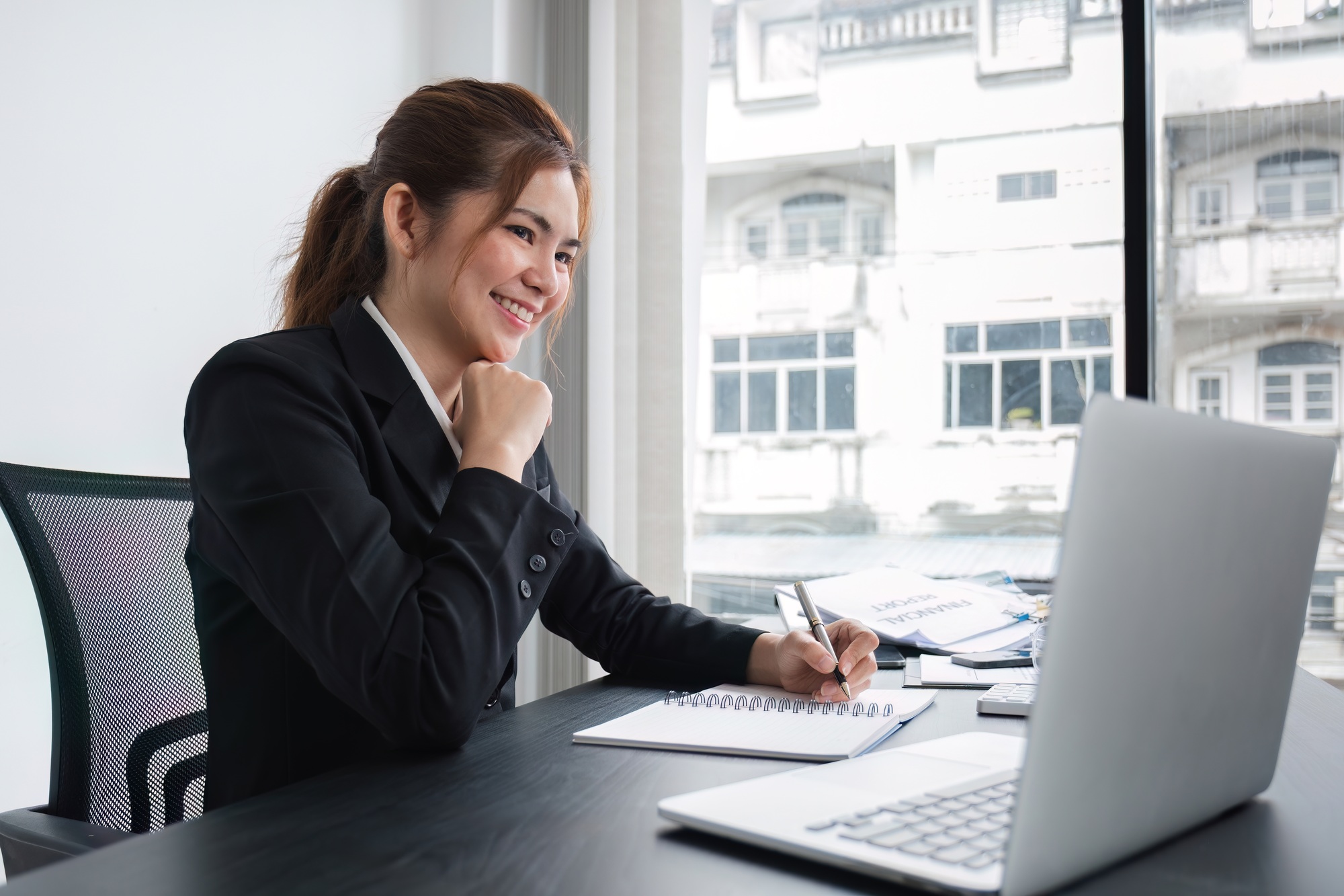 Attractive young businesswoman working using laptop on corporate charts and graphs on wooden table