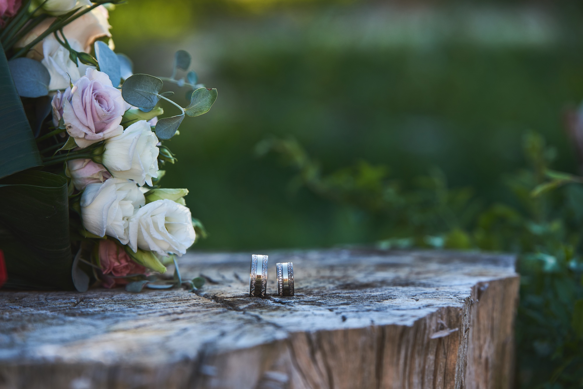 Closeup of wedding rings elegantly placed on a rustic wooden post with a bouquet of flowers