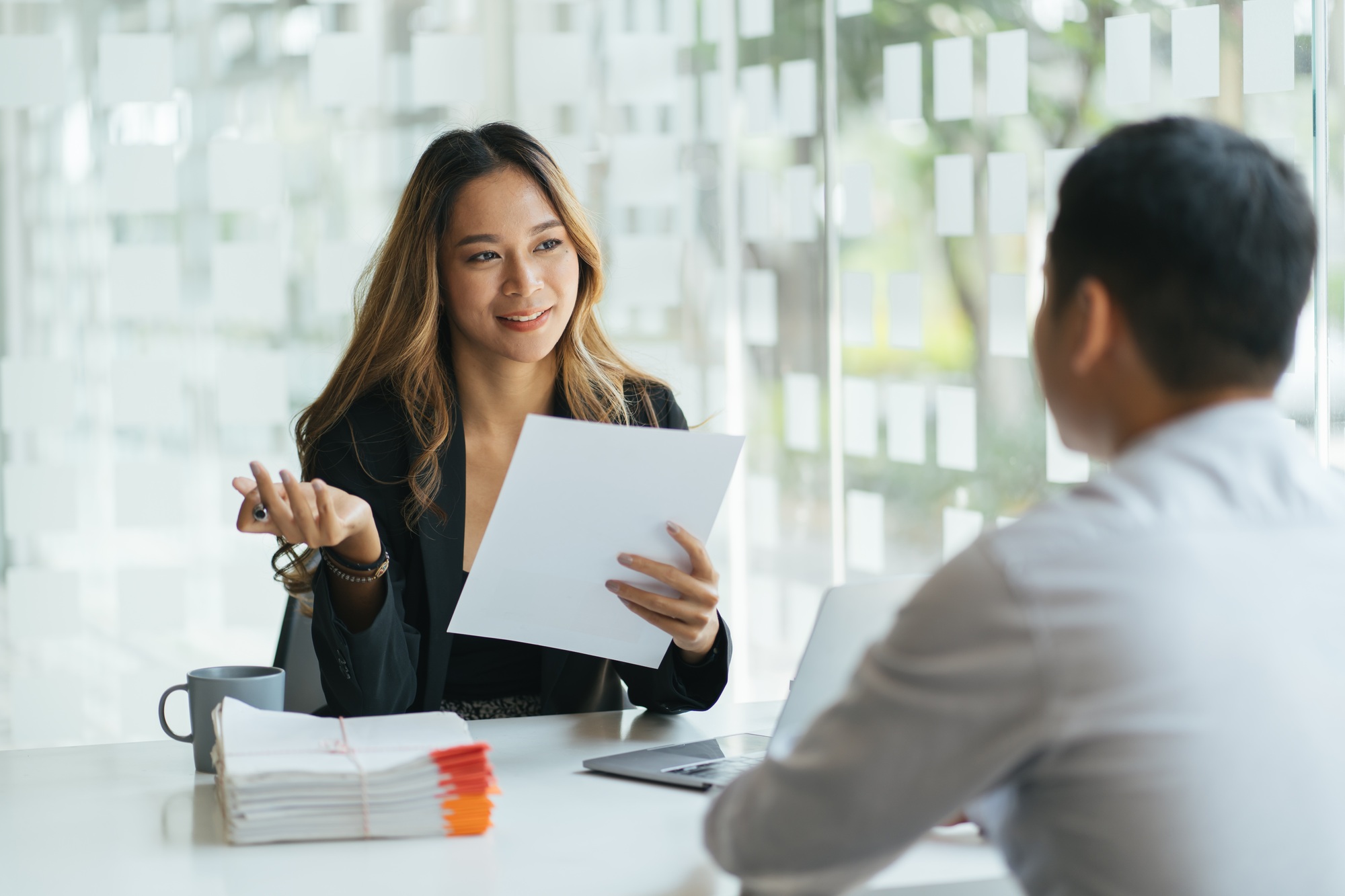 Joyful corporate trainer telling newcomer about work in company. Happy business woman holding table