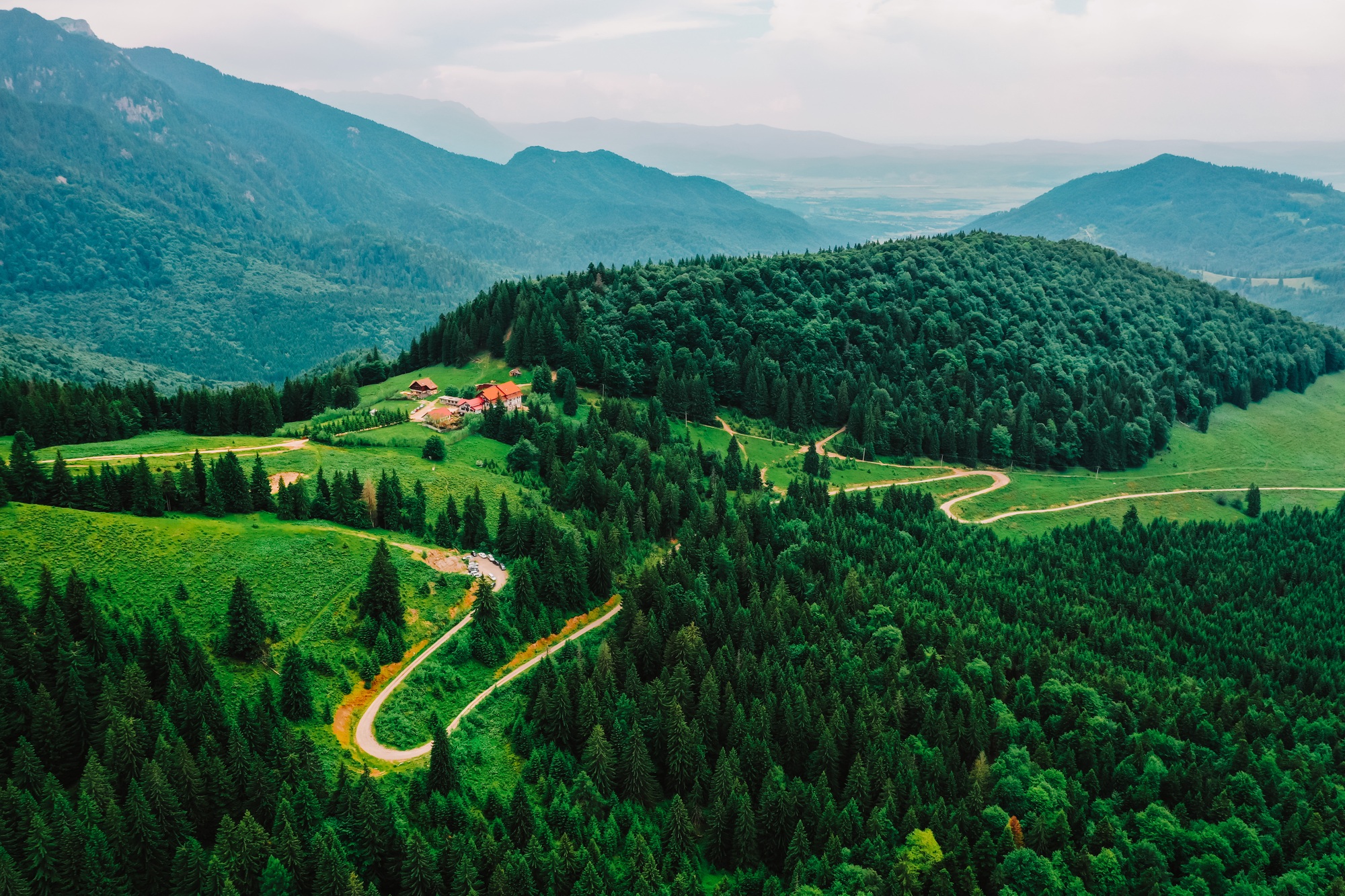 Natural drone photography with green forest and a tiny chalet surrounded by mountains and nature