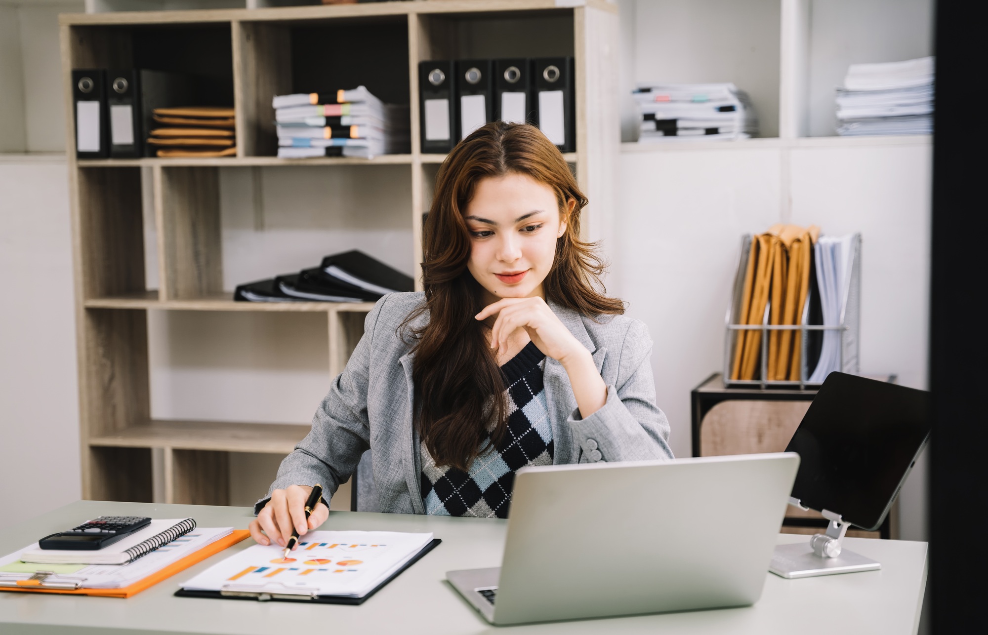 Portrait of Asian businesswoman working on laptop and papers on table in her office.